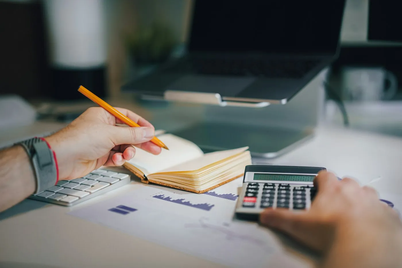Manos con lápiz y calculadora junto a un portátil